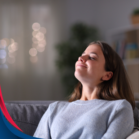 A young woman sits on a comfortable sofa, her head tilted back with a serene smile, enjoying the calm ambiance of her home.