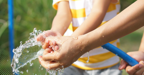 Washing hands outdoors with a garden hose.