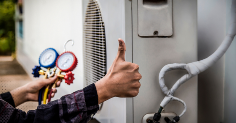 Technician giving a thumbs-up during HVAC system inspection, holding pressure gauges to check air conditioning performance.