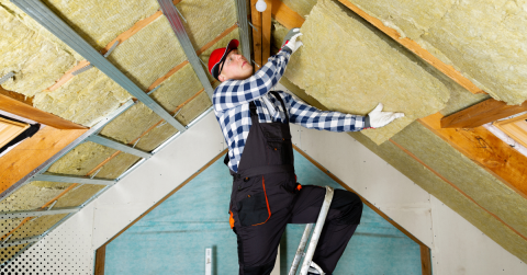 A worker installs insulation in an attic to improve energy efficiency and reduce heating costs.