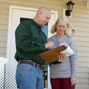 A home inspector and the homeowner go through the inspection report on a clipboard.