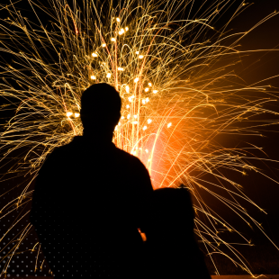 Vivid fireworks light up the sky behind a person's silhouette